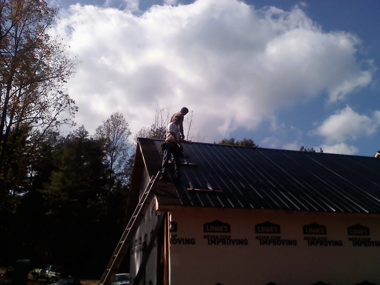 Roofer fastening dark metal panels high against a cloudy sky, from a Roof Inspection job in New Bedford